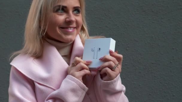 穿着粉色外套的年轻漂亮的金发女人在购物 这位女士拿着无线耳机包 从快乐中跳了出来 圣诞假期 零售业的理念 — 图库视频影像