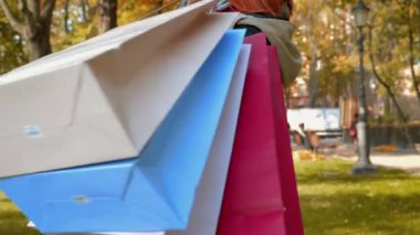 Ceketli, çekici, kızıl saçlı kadın alışveriş yapıyor. Parkta tilki gibi saçları olan bir kız çok renkli kağıt torbalarla alışveriş yapıyor. Satış, perakende sektörü konsepti. Yakın plan. 4k görüntü.