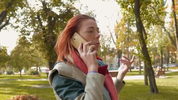 在停车场的红头发女人在用智能手机说话 带着狐狸毛的女孩在公园里散步 在电话里和一家网上商店的经理交谈 在网上下订单 零售业的概念 — 图库视频影像