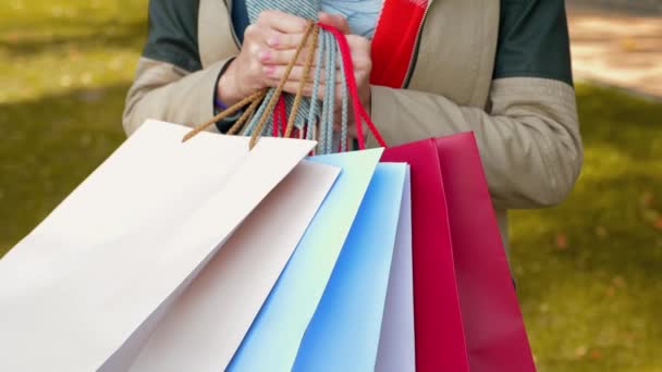 穿着夹克的年轻女人在购物 一个女孩站在公园里 用彩色纸袋购物 零售业的概念 4K镜头 — 图库视频影像