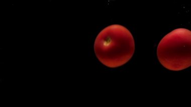 Siyah zemin üzerinde şeffaf suya düşen üç kırmızı domates. Akvaryuma taze organik sebzeler sıçrıyor. Market, sağlıklı yiyecekler, vejetaryenlik, hava kabarcıkları. Ağır çekim. Yakın plan..