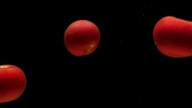 Siyah zemin üzerinde şeffaf suyun altında üç kırmızı domates yatıyor. Akvaryuma taze organik sebzeler sıçrıyor. Market, sağlıklı yiyecekler, diyet, vejetaryenlik, hava kabarcıkları. Ağır çekim. Yakın plan.