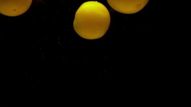 Siyah zemin üzerinde şeffaf suyun altında üç sarı domates yatıyor. Akvaryuma taze organik sebzeler sıçrıyor. Market, sağlıklı yiyecekler, vejetaryenlik, hava kabarcıkları. Ağır çekim. Yakın plan..