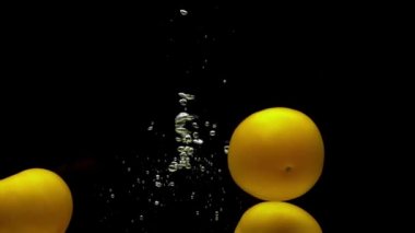 Siyah arka planda şeffaf suya düşen üç sarı domates. Akvaryuma taze organik sebzeler sıçrıyor. Market, sağlıklı yiyecekler, vejetaryenlik, hava kabarcıkları. Ağır çekim. Yakın plan..