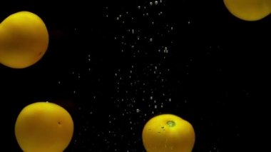 Siyah arka planda şeffaf suya düşen dört sarı domates. Akvaryuma taze organik sebzeler sıçrıyor. Market, sağlıklı yiyecekler, vejetaryenlik, hava kabarcıkları. Ağır çekim. Yakın plan..