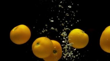 Siyah zemin üzerinde saydam suya düşen beş sarı domates. Akvaryuma taze organik sebzeler sıçrıyor. Market, sağlıklı yiyecekler, vejetaryenlik, hava kabarcıkları. Ağır çekim. Yakın plan..