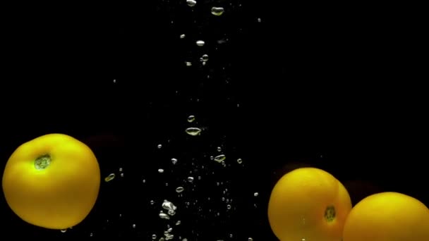 三个黄色的番茄在透明的水中掉在黑色的背景上 新鲜的有机蔬菜在水族馆里飞溅 杂货店 健康食品 素食主义 慢动作 后续行动 — 图库视频影像