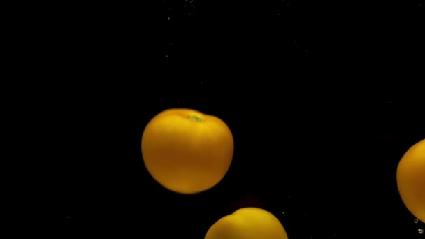 四个黄色的番茄在透明的水中掉在黑色的背景上 新鲜的有机蔬菜在水族馆里飞溅 杂货店 健康食品 素食主义 慢动作 后续行动 — 图库视频影像