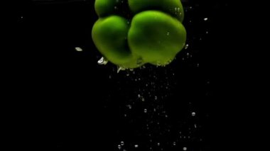 Siyah arka planda saydam suya düşen bir yeşil biber. Akvaryuma taze organik sebzeler sıçrıyor. Market, sağlıklı yiyecekler, diyet, vejetaryenlik, hava kabarcıkları. Ağır çekim. Yakın plan.
