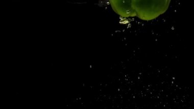 Siyah arka planda saydam suya düşen bir yeşil biber. Akvaryuma taze organik sebzeler sıçrıyor. Market, sağlıklı yiyecekler, diyet, vejetaryenlik, hava kabarcıkları. Ağır çekim. Yakın plan.