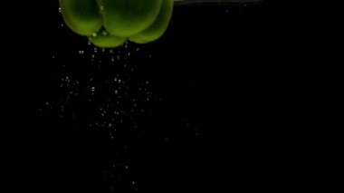 Siyah arka planda saydam suya düşen bir yeşil biber. Akvaryuma taze organik sebzeler sıçrıyor. Market, sağlıklı yiyecekler, diyet, vejetaryenlik, hava kabarcıkları. Ağır çekim. Yakın plan.