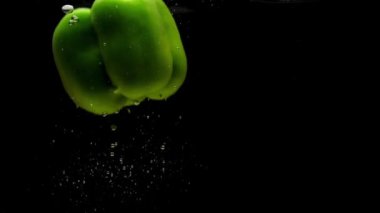 Siyah arka planda saydam suya düşen bir yeşil biber. Akvaryuma taze organik sebzeler sıçrıyor. Market, sağlıklı yiyecekler, diyet, vejetaryenlik, hava kabarcıkları. Ağır çekim. Yakın plan.