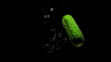Yeşil salatalık siyah arkaplanda saydam suya düşüyor. Akvaryuma taze organik sebzeler sıçrıyor. Market, sağlıklı yiyecekler, diyet, vejetaryenlik, hava kabarcıkları. Ağır çekim. Yakın plan..