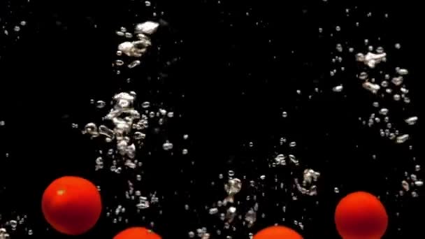 Tomates cerise rouge tombant dans l'eau transparente sur fond noir. Légumes biologiques frais éclaboussant dans l'aquarium. Épicerie, alimentation saine, régime alimentaire, végétarisme, bulles d'air. Gros plan sur le ralenti 