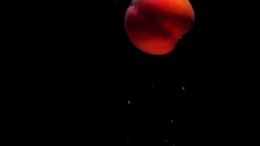 Olgun şeftali siyah zemin üzerinde şeffaf suya dökülüyor. Akvaryuma taze organik meyveler sıçrıyor. Market, sağlıklı yiyecekler, diyet, vejetaryenlik, hava kabarcıkları. Ağır çekim. Yakın plan..