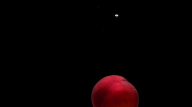 Olgun şeftali siyah zemin üzerinde şeffaf suya dökülüyor. Akvaryuma taze organik meyveler sıçrıyor. Market, sağlıklı yiyecekler, diyet, vejetaryenlik, hava kabarcıkları. Ağır çekim. Yakın plan..