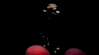 İki olgun şeftali, siyah arka planda şeffaf suya dökülüyor. Akvaryuma taze organik meyveler sıçrıyor. Market, sağlıklı yiyecekler, diyet, vejetaryenlik, hava kabarcıkları. Ağır çekim. Yakın plan..