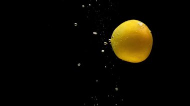 Olgun kayısı siyah zemin üzerinde şeffaf suya düşüyor. Akvaryuma taze organik meyveler sıçrıyor. Market, sağlıklı yiyecekler, diyet, vejetaryenlik, hava kabarcıkları. Ağır çekim. Yakın plan..