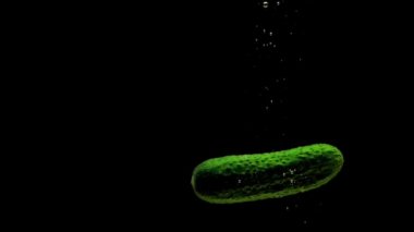 Yeşil salatalık siyah arkaplanda saydam suya düşüyor. Akvaryuma taze organik sebzeler sıçrıyor. Market, sağlıklı yiyecekler, diyet, vejetaryenlik, hava kabarcıkları. Ağır çekim. Yakın plan..