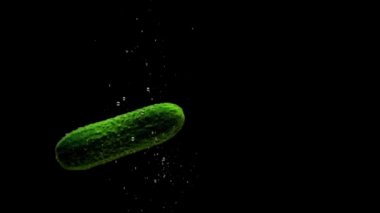 Yeşil salatalık siyah arkaplanda saydam suya düşüyor. Akvaryuma taze organik sebzeler sıçrıyor. Market, sağlıklı yiyecekler, diyet, vejetaryenlik, hava kabarcıkları. Ağır çekim. Yakın plan..