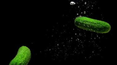 Yeşil salatalıklar siyah arkaplanda saydam suya düşüyorlar. Akvaryuma taze organik sebzeler sıçrıyor. Market, sağlıklı yiyecekler, diyet, vejetaryenlik, hava kabarcıkları. Ağır çekim. Yakın plan.