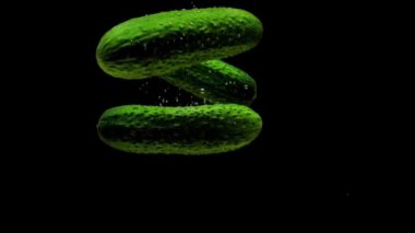 Yeşil salatalıklar siyah arkaplanda saydam suya düşüyorlar. Akvaryuma taze organik sebzeler sıçrıyor. Market, sağlıklı yiyecekler, diyet, vejetaryenlik, hava kabarcıkları. Ağır çekim. Yakın plan.