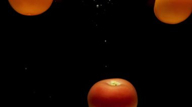 Kırmızı ve sarı domatesler siyah arkaplanda saydam suya düşüyorlar. Akvaryuma taze organik sebzeler sıçrıyor. Market, sağlıklı yiyecekler, vejetaryenlik, hava kabarcıkları. Ağır çekim. Yakın plan..