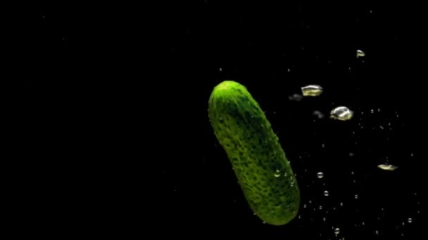 绿黄瓜在黑色的背景上掉进透明的水里 新鲜的有机蔬菜在水族馆里飞溅 杂货店 健康食品 空气泡泡 慢动作 后续行动 — 图库视频影像