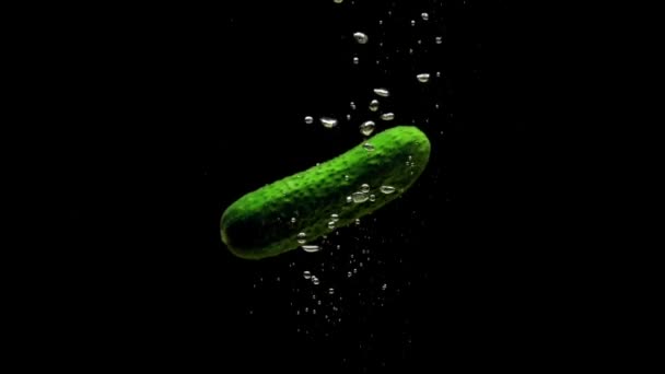 绿黄瓜在黑色的背景上掉进透明的水里 新鲜的有机蔬菜在水族馆里飞溅 杂货店 健康食品 空气泡泡 慢动作 后续行动 — 图库视频影像