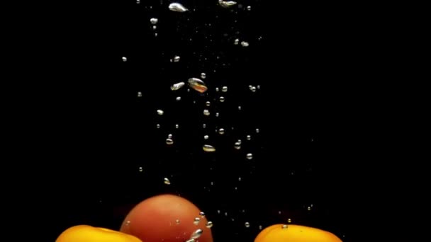 红色和黄色的番茄在透明的水中落在黑色的背景上 新鲜的有机蔬菜在水族馆里飞溅 杂货店 健康食品 素食主义 慢动作 后续行动 — 图库视频影像