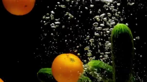 トマトとキュウリは黒い背景の透明な水に落ちます 新鮮な有機野菜が水族館で飛び散っています 食料品店 健康食品 食事菜食主義 スローモーションクローズアップ — ストック動画