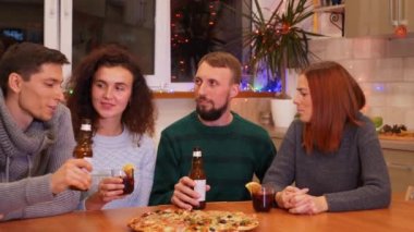 Mutlu arkadaşlar kadeh tokuşturup yeni yıl partisini evde kutluyorlar. Pizza, bira şişeleri ve masada sıcak şarap. Tatiller ve kutlama konsepti. 4k görüntü.