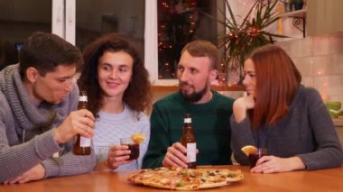 Arkadaşlar yeni yıl partisini evde kutluyor, kadeh tokuşturup kadeh tokuşturuyorlar. Pizza, bira şişeleri ve masada sıcak şarap. Tatiller ve kutlama konsepti. 4k görüntü.