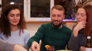 Happy friends talking, eating pizza, drinks alcohol and celebrating new years eve party at home. Bottles of beer and glasses of mulled wine on the table. Holidays and celebration concept. 4K footage.