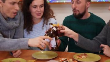 Mutlu arkadaşlar kadeh tokuşturup yeni yıl partisini evde kutluyorlar. Pizza, bira şişeleri ve masada sıcak şarap. Tatiller ve kutlama konsepti. 4K görüntü. Yakın plan..