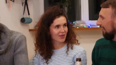 Mutlu arkadaşlar şenlik masasında konuşuyorlar ve evde yeni yıl partisini kutluyorlar. Pizza, bira şişeleri ve masada sıcak şarap. Tatiller ve kutlama konsepti. 4k görüntü.