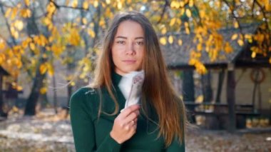 Genç, çekici, esmer bir kadın yüzüne bir para yelpazesi sallıyor. Bir kız çok paradan hoşlanır. Büyük bir servet. Çalışan maaşı. Nakit para ödemesi. Başarılı iş konsepti. 4k görüntü.