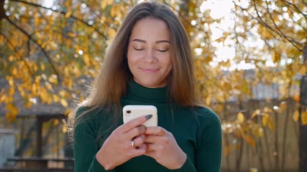 Akıllı Telefon Kullanan Sonbaharda Sarı Ağaçların Arka Planında Gülümseyen Komik — Stok video