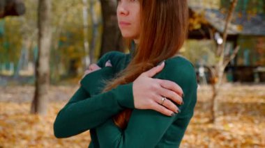 Donmuş genç, çekici esmer kadın sonbaharda sarı ağaçların arka planında parkta yürüyor. Güneşli bir günde yeşil kazaklı güzel bir kız ormanın ortasında geziniyor. Yakın plan. 4k