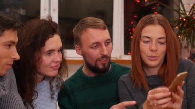 Arkadaşlarına fotoğraflarını gösteren hanımefendinin yakın plan fotoğrafları, akıllı telefondan çekilmiş videoları. Mutlu arkadaşlar telefonla izliyor, şenlik masasında konuşuyor ve evde yeni yıl partisini kutluyorlar. Tatil konsepti. 4k