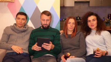 Mutlu arkadaşlar kanepede oturuyor, tablet kullanıyor ve evde yeni yıl partisini kutluyorlar. Çok renkli ışıklar, arka planda çelenkler. Tatiller ve kutlama konsepti. 4k görüntü.