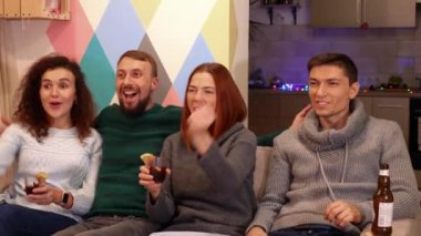 Mutlu arkadaşlar kanepede oturuyor, alkol içiyor ve yeni yıl tatillerinde TV 'de kış sporu maçı izliyorlar. Arka planda çok renkli duvar var. Tatiller ve kutlama konsepti. 4k görüntü.