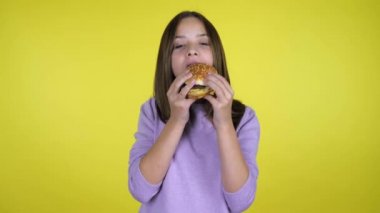 Pembe kazaklı genç kız sarı arka planda fotokopi alanı olan bir burger yiyor.