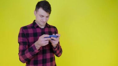Neşeli adam, sarı arka planda akıllı telefondan hevesle video oyunu oynuyor.