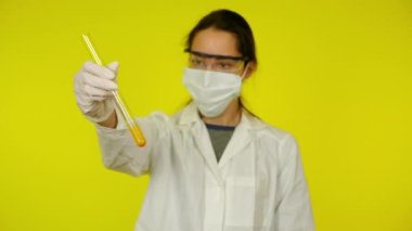 Beyaz elbiseli kadın, koruyucu maske test tüpünün içindekileri inceliyor.
