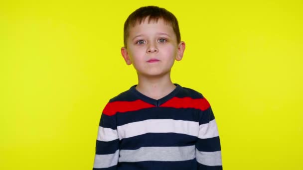 Komoly kisgyerek néz a kamerába, és mosolyog a sárga háttér — Stock videók