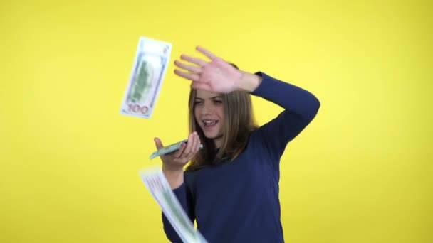 有钱的少女把很多钱扔在黄色的背景上笑了 — 图库视频影像