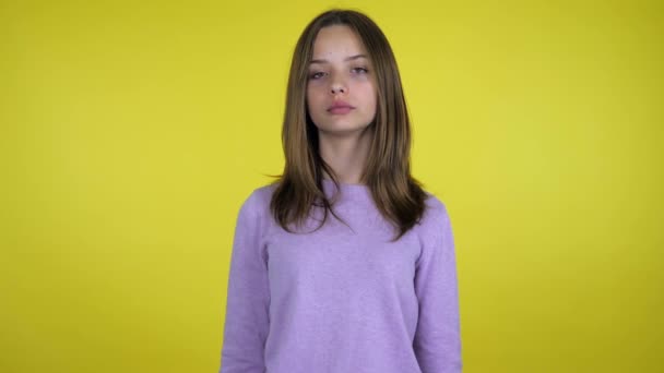 Tiener meisje in een roze trui kijkt naar de camera op een gele achtergrond — Stockvideo