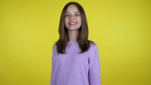 Tiener meisje in een roze trui draait naar de camera en glimlacht op gele achtergrond — Stockvideo
