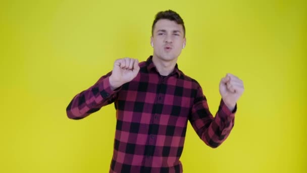Homem ouve música em fones de ouvido sem fio e dança em um fundo amarelo — Vídeo de Stock